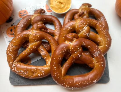 Five pretzel twists in the shape of pumpkins with nacho cheese, a pumpkin and a halloween napkin on a counterop.